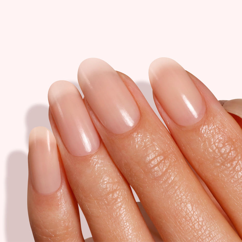 Close-up of a hand with glossy, well-manicured nails showing a hint of Apricot Beige from LONDONTOWN's Tinted Fortifying Ridge Filler against a light background.