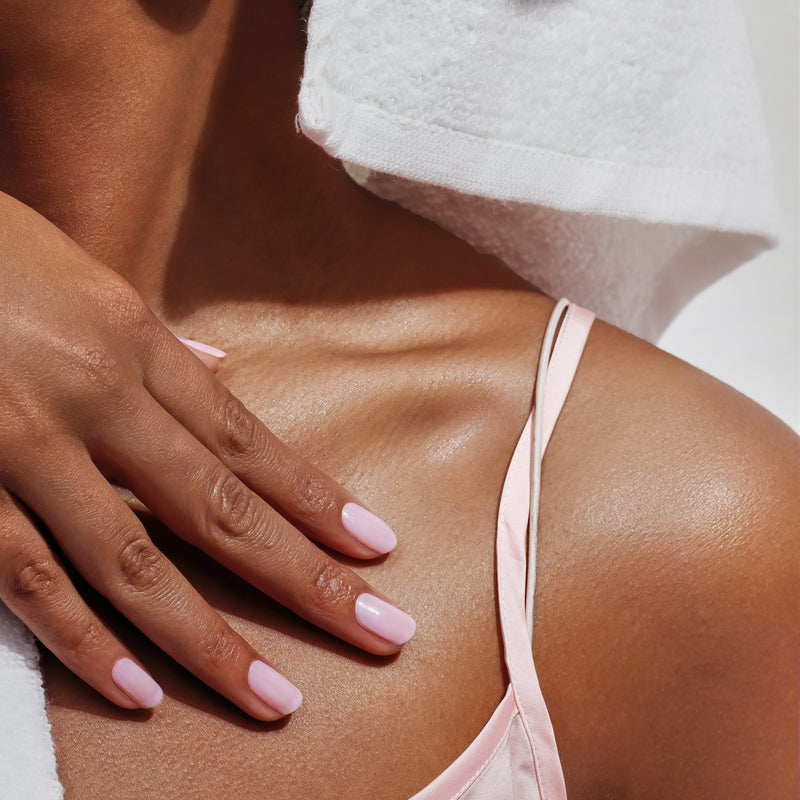 Close-up of a person’s shoulder with Magnolia Haze nail polish by LONDONTOWN, wearing a versatile pink strap and a white towel draped over their head.