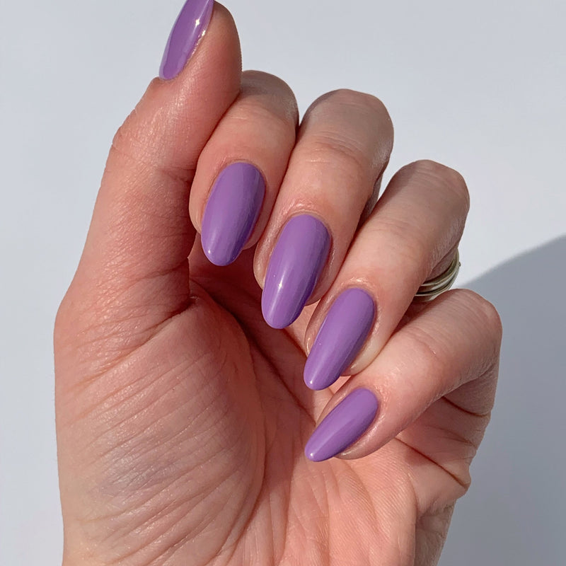 A hand with long, almond-shaped nails painted in LONDONTOWN's glossy "Road Trip" lavender shade is shown against a light background.