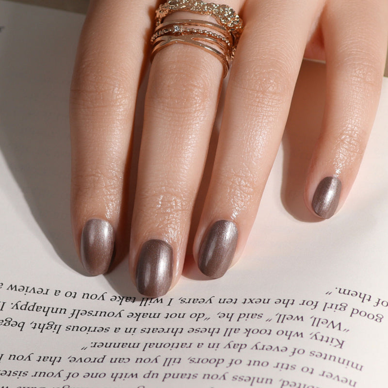 A hand featuring LONDONTOWN's Gel Genius Base Coat rests on an open book, its fingers adorned with several gold rings.
