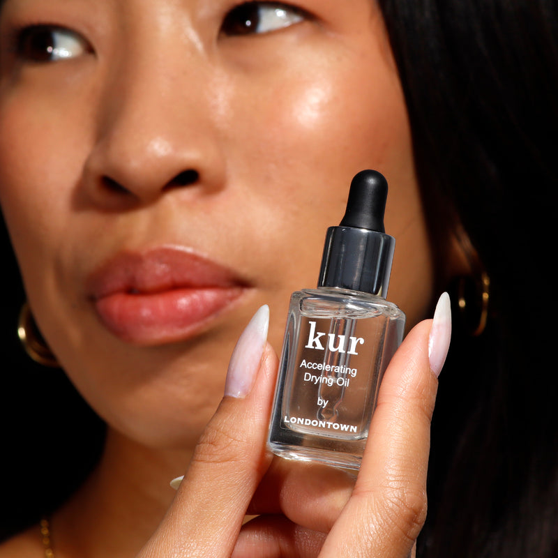 A person holds a bottle of LONDONTOWN Accelerating Drying Oil, a quick-drying solution enriched with nourishing botanical oil.