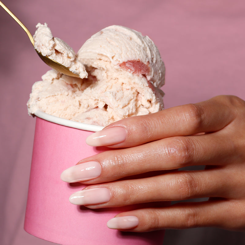 A manicured hand holds LONDONTOWN's Double Scoop, a creamy pink ice cream, and scoops out a serving with a spoon.