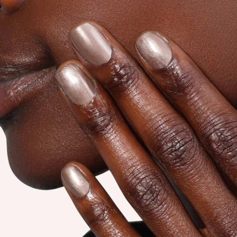 A person gently touches their cheek, highlighting the stunning Nightcap bronze metallic nail polish by LONDONTOWN on their fingers.