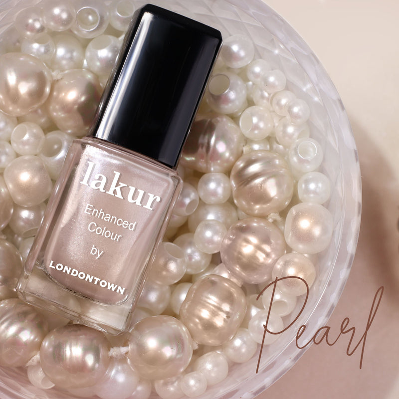 A bottle of LONDONTOWN's Lakur nail polish called "Pearl" is elegantly surrounded by decorative pearls, echoing a soft and shimmering allure reminiscent of champagne's grace.