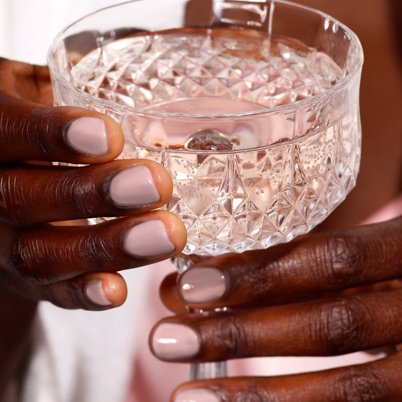 Hands elegantly displaying LONDONTOWN's "Do Not Disturb" nail polish gently cradle a crystal glass filled with a clear liquid.