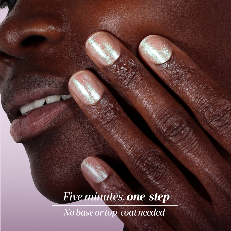 A close-up of a person’s face and hand, featuring LONDONTOWN’s Shimmering Nail Highlighter in Stardust. Get salon-quality, shimmery pink nails in five minutes with this one-step polish—no base or top coat needed.