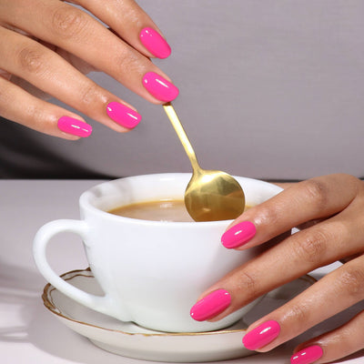 Close-up of hands with LONDONTOWN's GelShift Top Coat holding a white cup and stirring with a gold spoon.