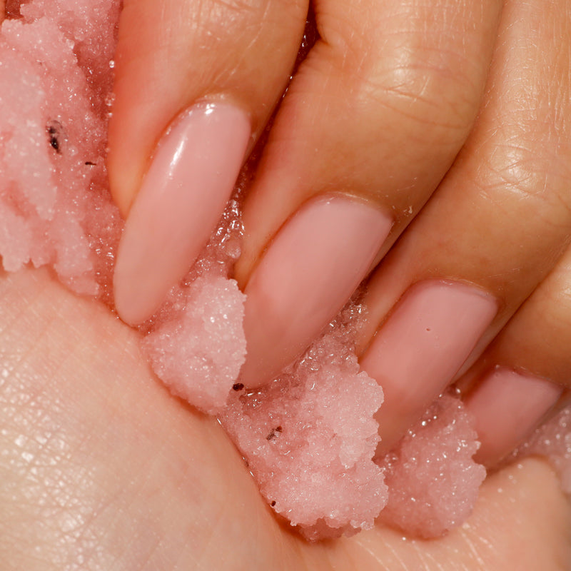 A close-up of a hand with long, pink manicured nails holding LONDONTOWN's Soft Touch Nail Scrub highlights beauty and care in perfect harmony.