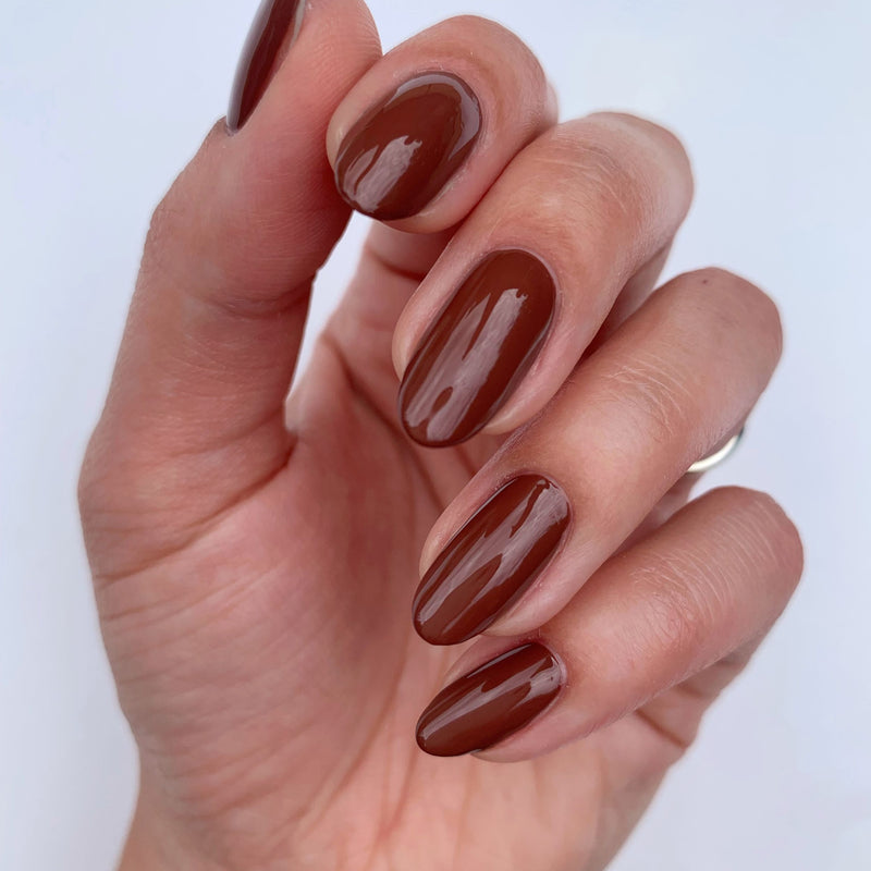 Close-up of a hand with smooth, glossy nails in LONDONTOWN's Oud Mood color against a light background.