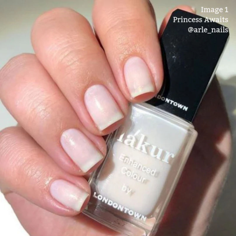 A hand holds a bottle of LONDONTOWN nail polish labeled "Princess Awaits," featuring a sheer white shimmer. The vegan, cruelty-free polish boasts a 16+ Free formula for conscious beauty lovers, while the nails glow beautifully in their soft, pale shade.
