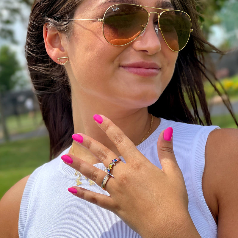 A woman wearing sunglasses and a white top displays her colorful rings and vibrant Berry Punch vegan, cruelty-free nail polish by LONDONTOWN, proudly made in the USA, outside.