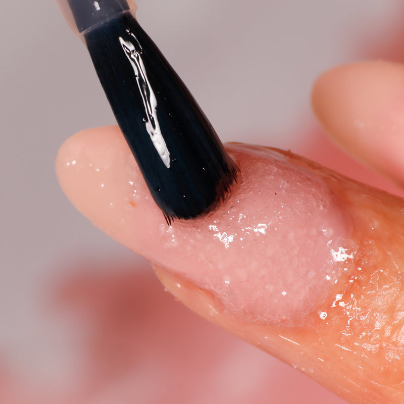 Close-up of a brush applying LONDONTOWN's Soft Touch Nail Scrub onto a person's fingernail.