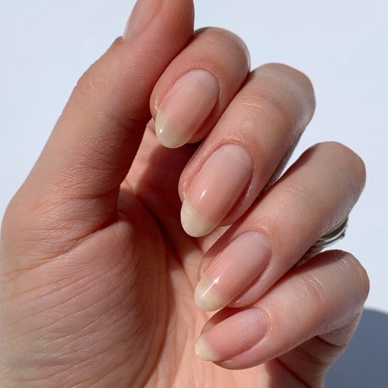 A close-up shows a hand with neatly filed, natural nails adorned in LONDONTOWN's Cheerio, a sheer neutral pink, under bright lighting.