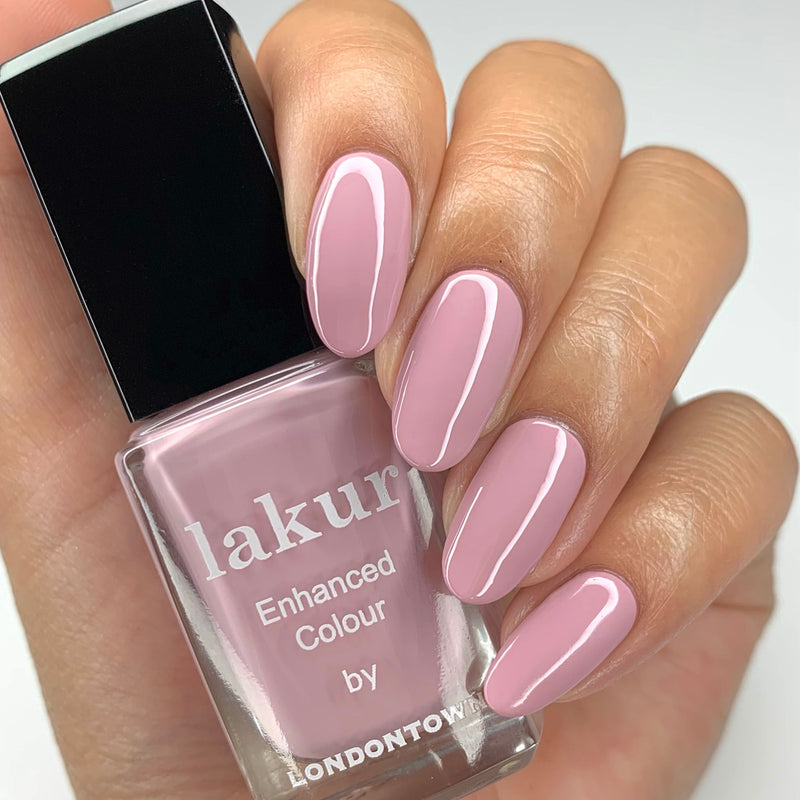 A hand elegantly showcases glossy light pink nail polish while holding a bottle labeled "Berry Nude" by LONDONTOWN. This delectable blend of colors, reminiscent of blueberry-tinted whipped cream, offers a chic and sophisticated look.