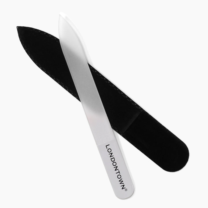 A clear glass nail file from LONDONTOWN, featuring a white handle, is positioned diagonally beside a black protective case on a white background, offering effortless and damage-free nail filing.