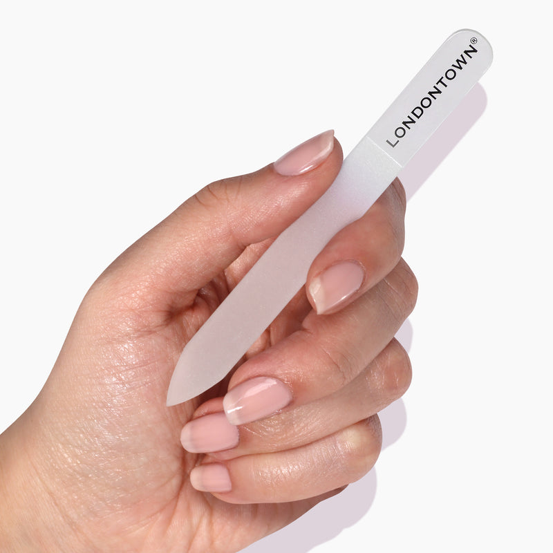 A hand with neatly manicured nails holding a Glass Nail File - Clear labeled "LONDONTOWN," showcasing effortless nail filing without risk of damage.