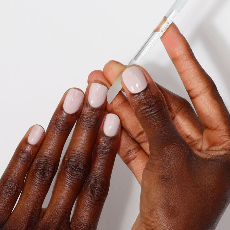 Two hands are shown; one holding the LONDONTOWN Glass Cuticle Pusher is near the neatly manicured, lightly polished nails of the other.