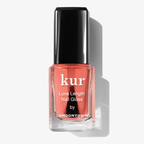 A clear glass bottle of LONDONTOWN Luxe Length Nail Gloss with a black cap, containing coral-pink polish that protects and supports nail growth.