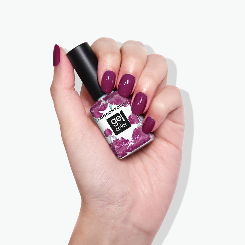 Hand with purple manicured nails holding a bottle of LONDONTOWN Violet Hibiscus Gel Color nail polish, enhanced with deep ultraviolet technology for an enduring shine.
