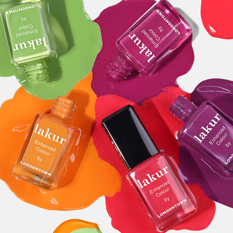Four bottles of LONDONTOWN's Heat Wave nail polish in various colors are shown spilling onto a white surface, creating colorful splashes. The vibrant hues include green, burnt orange, pink, and purple.