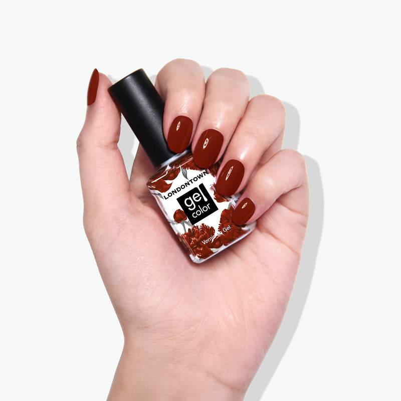A hand with manicured nails holds a bottle of LONDONTOWN's "You Autumn Know" gel nail polish in a rich umber shade.