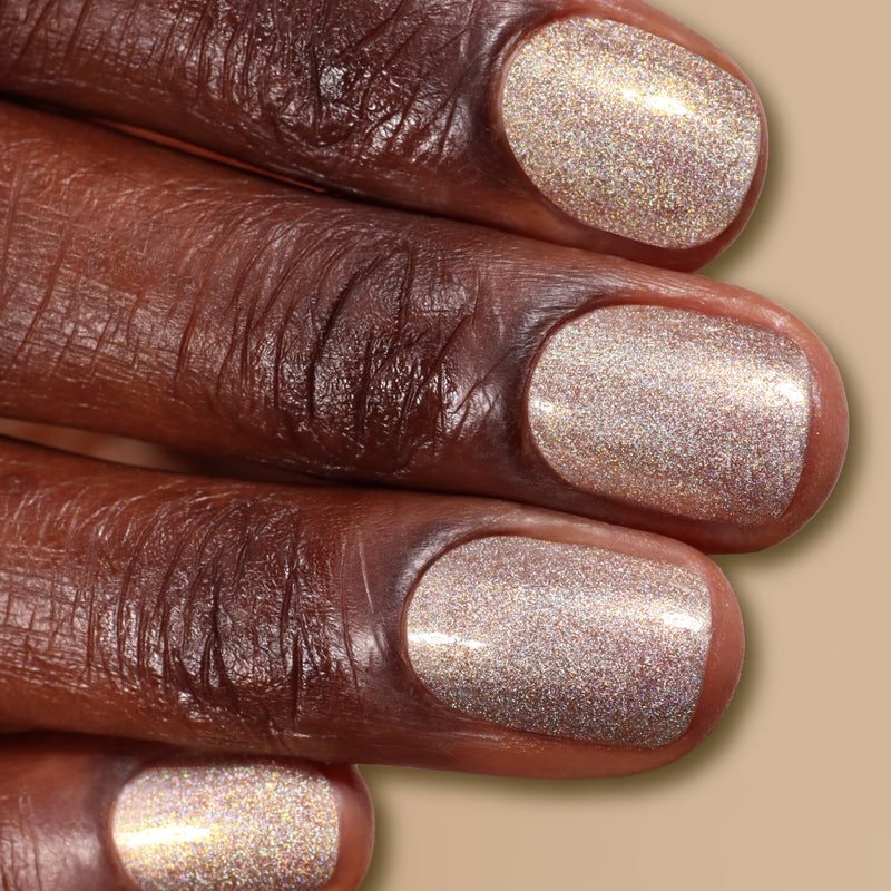 Close-up of four fingers with short, neatly filed nails painted in LONDONTOWN's You're Golden, a shimmery, holographic silver and gold nail polish.