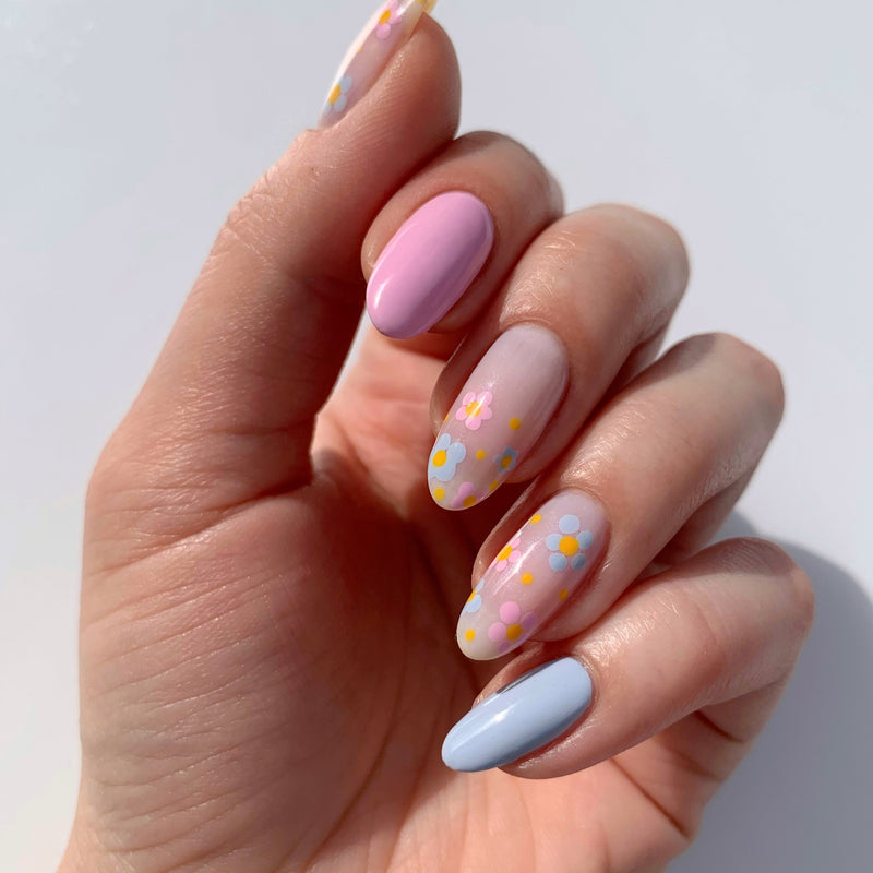 A hand with long, almond-shaped nails is painted in pastel colors—light pink, lavender, and light blue—and one nail displays a professional design featuring colorful dot flower patterns created using the Dot & Detail Nail Art Tool by LONDONTOWN.