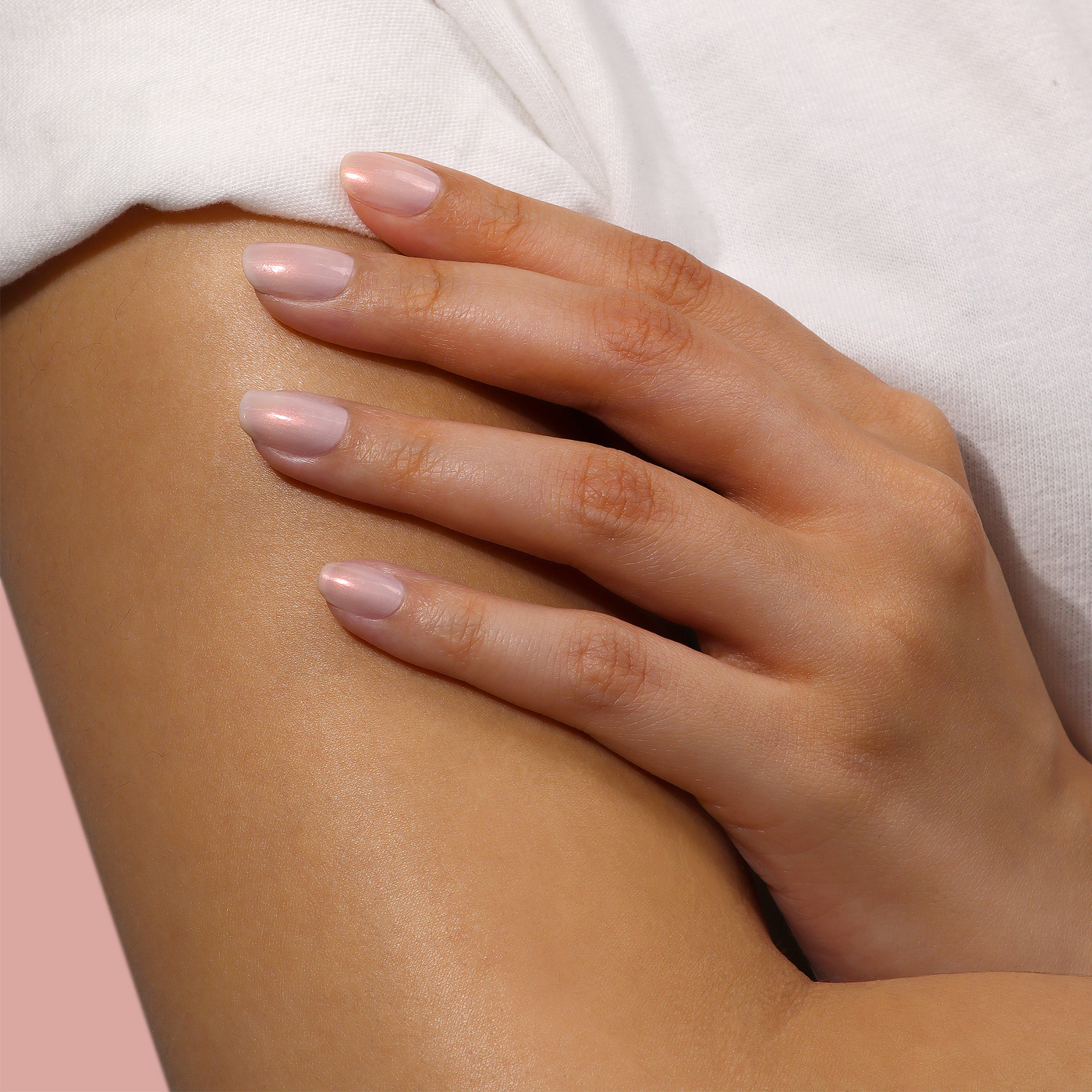 A hand with manicured nails, coated in LONDONTOWN's Bubble Illuminating Nail Concealer (Professional), rests on an arm against a pink background.