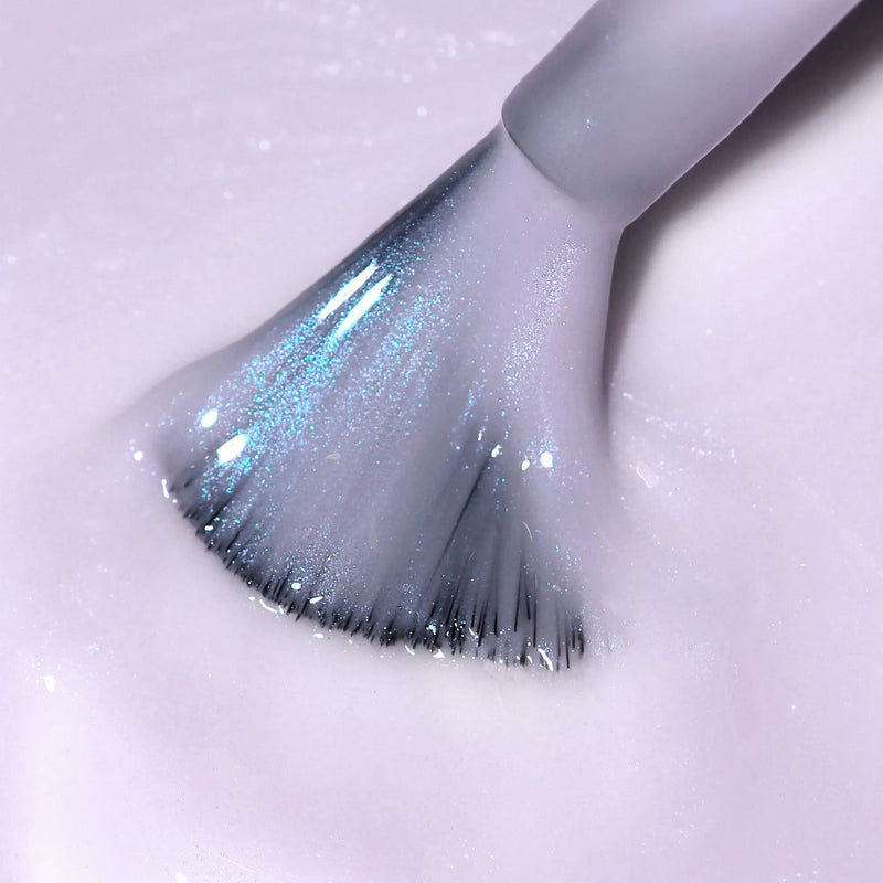 A close-up of LONDONTOWN's Lavender Illuminating Nail Concealer brush with silver-blue bristles coated in shimmery lavender polish, delivering a perfecting formula for flawless application.