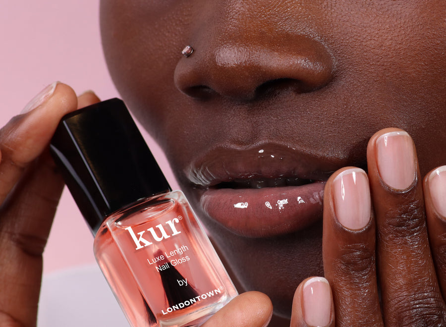 Model holding a bottle of Luxe Length Nail Gloss beside glossy lips