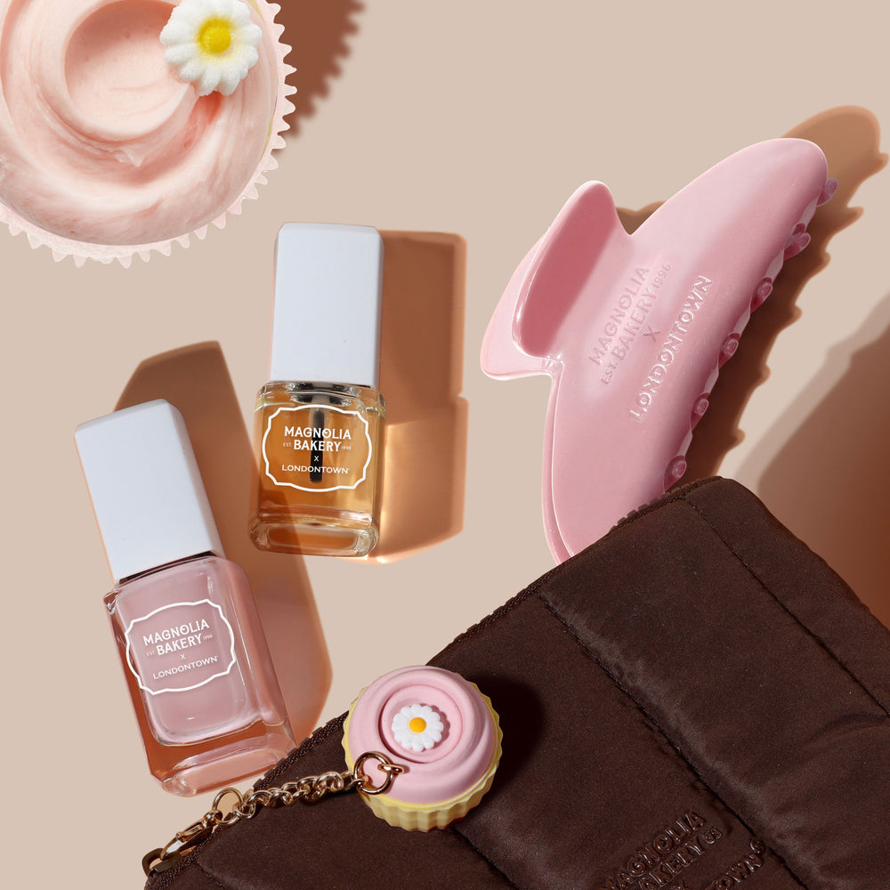The Sweet Essentials Bag Set by LONDONTOWN includes two nail polishes (clear and pink), a cupcake, a pink hair clip, and a brown pouch, all artfully displayed on a beige surface.