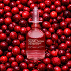 A bottle of LONDONTOWN Peptide Serum Concentrate, designed for nail repair and cuticle care, is set against a backdrop of fresh red cranberries.