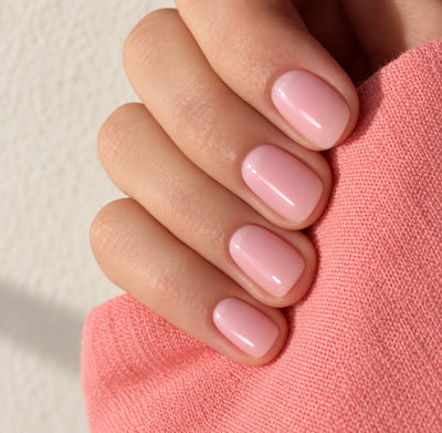 Hand with glossy pink natural nails resting on a coral knit