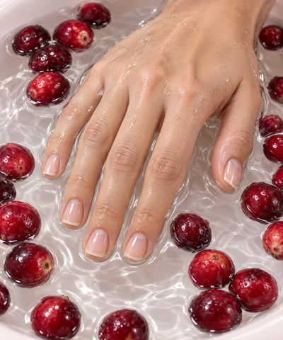 Hand with bare natural nails resting in water among cranberries