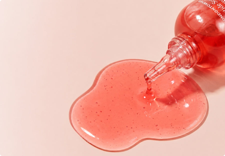Drops of pink LONDONTOWN Peptide Serum Concentrate pooling from the bottle tip