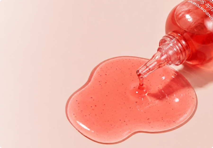 Peptide Serum Concentrate bottle dispensing pink gel serum on a blush background