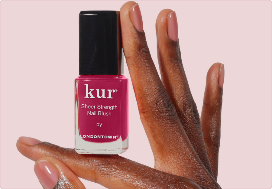Hand holding a bottle of kur Sheer Strength Nail Blush in Hibiscus against a soft pink background
