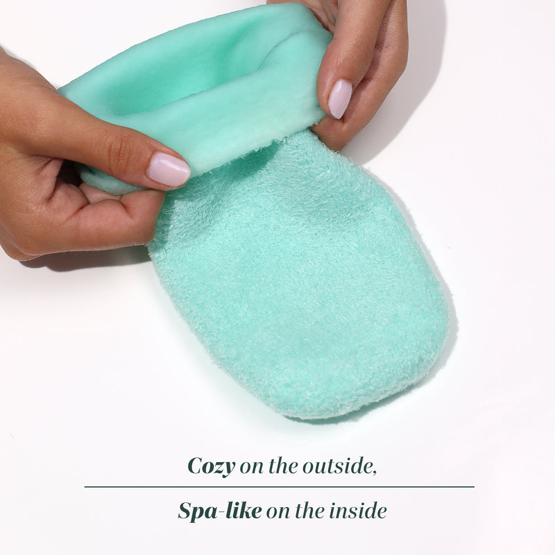 A person holds open a soft, mint-green slipper with plush lining; text below reads, "Pedi Perfect Moisturizing Spa Socks by LONDONTOWN—cozy on the outside, spa-like on the inside.