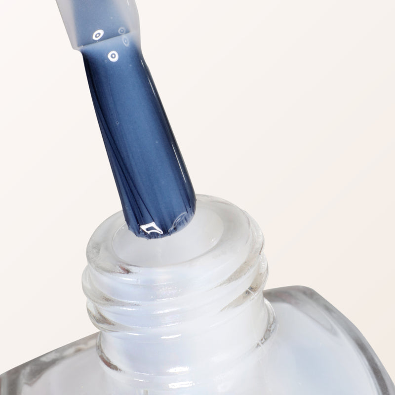 Close-up of a nail polish brush with blue Fresh Glow Cuticle Remover by LONDONTOWN being pulled out of a clear bottle, ready to perfect nails and hydrate overgrown cuticles.