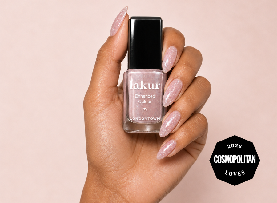 Hand holding a bottle of lakur in Champagne in Bed with matching manicure, Cosmopolitan Loves 2025 badge