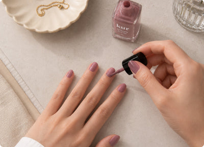 Hand applying a sheer mauve nail veil next to the bottle