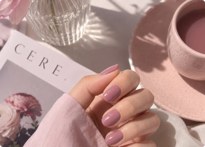 Hand with sheer mauve nails resting on a magazine beside a pink cup