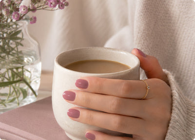 Hands with sheer mauve nails holding a cup of coffee