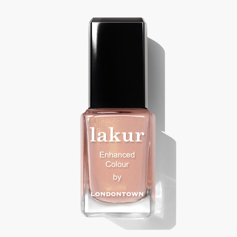 A bottle of LONDONTOWN's Lakur enhanced color nail polish in the shade Amber Lights, featuring a light peachy-pink tone reminiscent of a sunset, set against a plain white background.