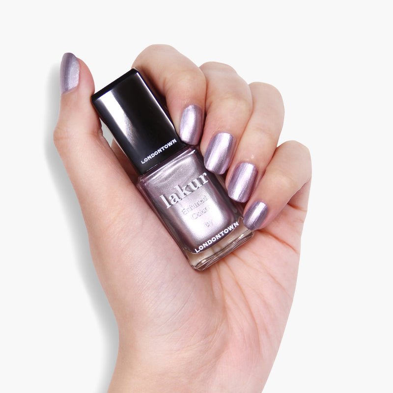 A hand holding a bottle of LONDONTOWN BRILL-ant vegan cruelty-free nail polish with metallic purple nail polish applied on the fingernails.