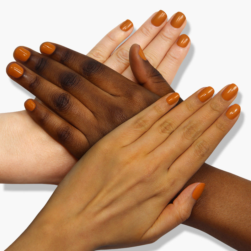 Four overlapping hands with different skin tones displaying freshly manicured nails, each painted in the robust shade of goldenrod orange from LONDONTOWN's Bee's Knees collection.
