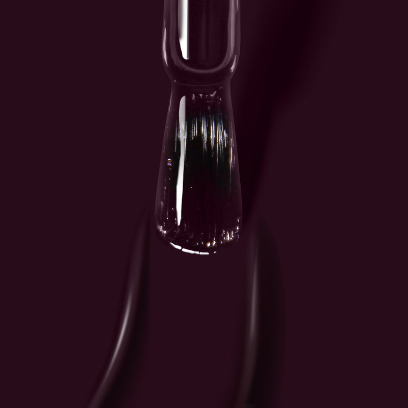 Close-up of the LONDONTOWN Bell in Time nail polish brush dipped in a dark, glossy, deep purple cream. The blurred background emphasizes the high-shine formula on the brush and polish.