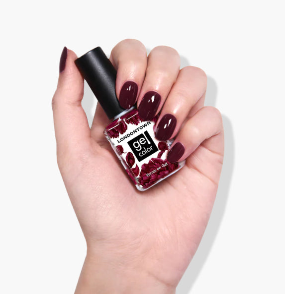 A hand with dark red gel nail polish holds a LONDONTOWN Bell in Time UV/LED Gel Color bottle against a white background.