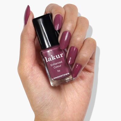 A hand displaying manicured nails coated in a dreamy, dusty rose nail polish holds a bottle of LONDONTOWN Best Year Ever (Professional) nail lacquer.