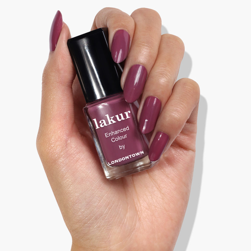 A hand with painted nails holds a bottle of LONDONTOWN nail polish in the dreamy purple shade labeled "Best Year Ever.